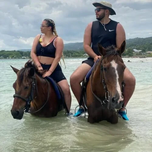 Two guests horseback riding in shallow Caribbean water